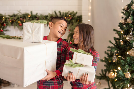 Laughing kids holding gifts in front of christmas tree