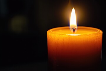 A lit cylindrical wax candle emitting a soft warm glow isolated on a white background
