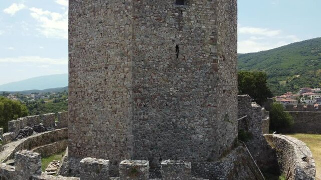 A medieval stone tower nestled within a historic castle complex. Vibrant greenery and turquoise waters of the Mediterranean coastline. Ancient architecture with the serene beauty of the sea.