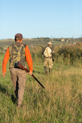 Mature hunter man holding a shotgun and walking through a field