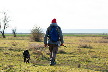 Mature hunter man holding a shotgun and walking through a field