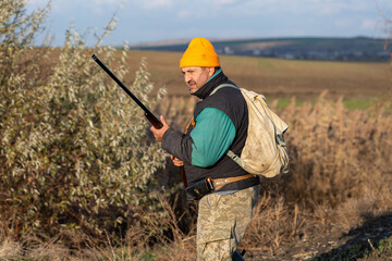 Mature hunter man holding a shotgun and walking through a field