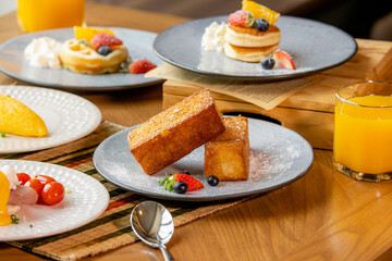 A vibrant breakfast spread featuring French toast, pancakes, fresh fruits, and orange juice on wooden tables.