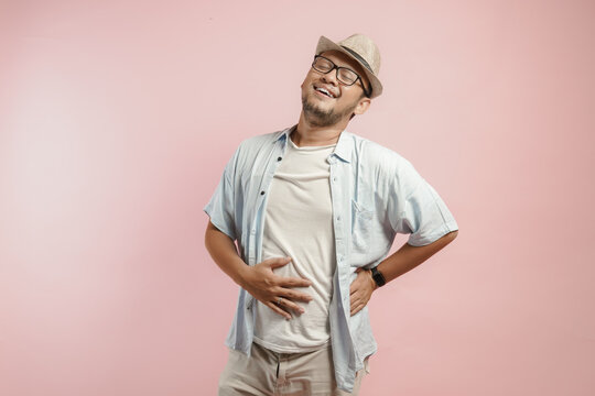 Peaceful young Asian man wearing hat and blue shirt holding his stomach with a relief expression.