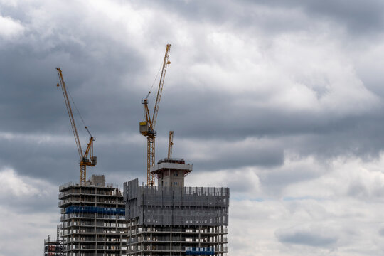 A dramatic scene featuring towering cranes at a construction site under brooding skies, representing industrial development and the evolution of urban landscapes in London UK
