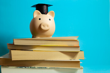 Piggy bank with mortarboard on stacked books in a blue isolated background, tuition savings concept