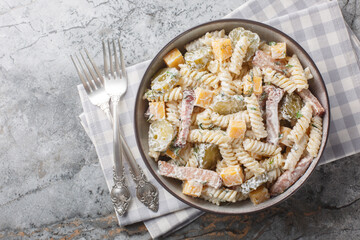 Winter delicious pasta salad with pickles, yellow cheese, herbs and bacon seasoned with mayonnaise close-up in a bowl on the table. Horizontal top view from above