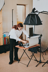 Female photographer taking photo of objects on background in photo studio with professional equipment