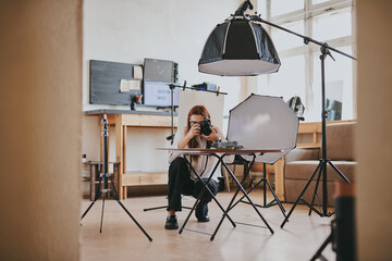 Female photographer taking photo of objects on background in photo studio with professional...