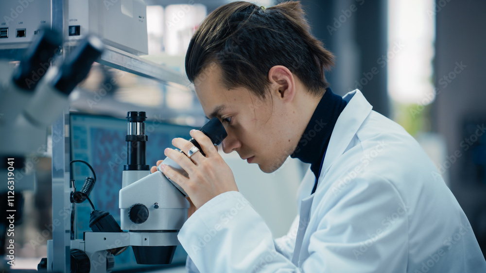 Poster portrait of a young graduate student working in a laboratory, using advanced microscope, writing dow