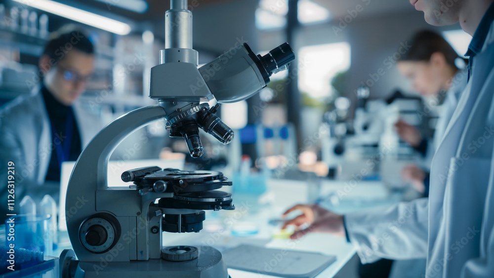 Poster close up portrait of a young microbiologist wearing glasses and looking through the microscope, anal