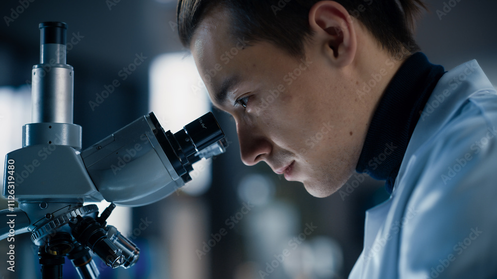 Poster Portrait of a Handsome Chemistry Student Working on a Research Project in University. Medical Research Scientist Looking at Biological Samples Under a Microscope in an Applied Science Laboratory
