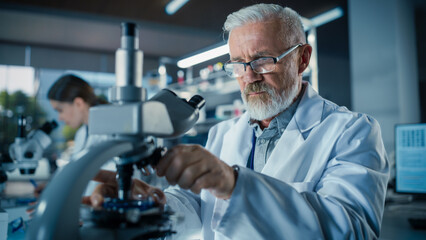 Senior Medical Research Scientist Looking at Biological Samples Under a Microscope in an Applied Science Laboratory. Portrait of a Handsome Middle Aged Doctor Working on a Research Project