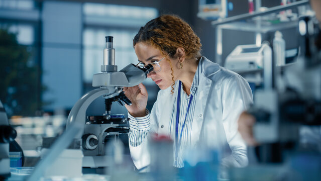Portrait of a Multiethnic Student Working on a Research Project in College. Medical Research Scientist Looking at Biological Samples Under a Microscope in an Applied Science Laboratory - Powered by Adobe