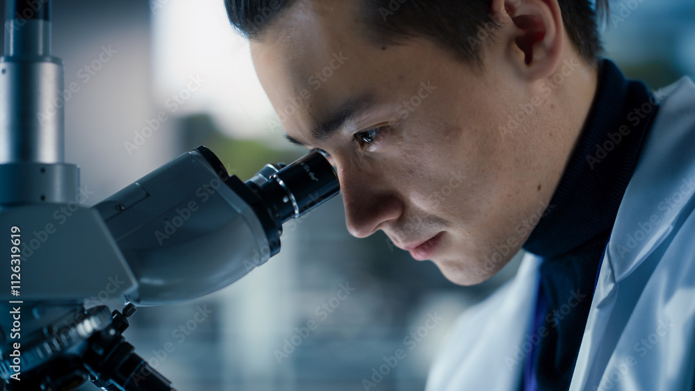Poster Portrait of a Handsome Chemistry Student Working on a Research Project in University. Medical Research Scientist Looking at Biological Samples Under a Microscope in an Applied Science Laboratory