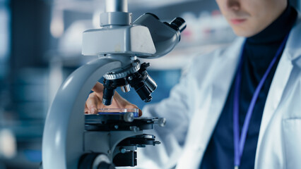 Medical Research and Development Laboratory: Close Up of a Male Scientist Preparing a Biological Sample in a Petri Dish in a Microscope in an Advanced Biotechnology Lab