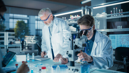 Head of Laboratory Making a Bioengineering Experiment with a Group of Young Science College Students. Future Specialists Working with Modern Microscopes, Using Tablet and Laptop Computers