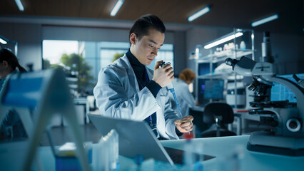 Biology Research Scientist Applying a Molecular Sample with a Micro Pipette and Researching Under a Microscope in a Science Laboratory. Young Lab Engineer in White Coat Working on Vaccine Products