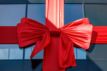 Large red ribbon, tied in a bow, drapes across a modern building's window.  A grand opening or...