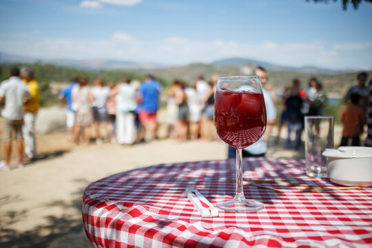 Outdoor picnic scene;  red wine drink on a checkered tablecloth.  Group of people in the background.