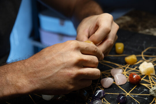 Male hands holding various fortune telling multicolored natural stones in a dark room of accult purpose. Fortune tellers magicians and esoterics
