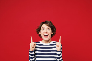 Young surprised shocked happy woman she wear blue striped sweatshirt casual clothes point index finger overhead on empty area mockup isolated on plain red background studio portrait Lifestyle concept