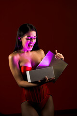 Sexy woman in a red bodysuit posing with a gift on a red background. Gift in the hands of an attractive woman. Christmas concept. Christmas gift