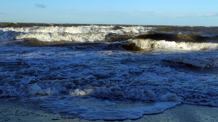 Fototapeta premium Stormy sea with dark waves crashing against the shore under a cloudy sky during late afternoon