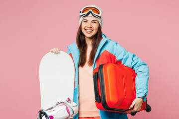 Traveler winner woman wear blue padded jacket ski goggles mask hold snowboard bag isolated on plain pink background. Tourist travel abroad in free time rest getaway. Air flight trip journey concept.