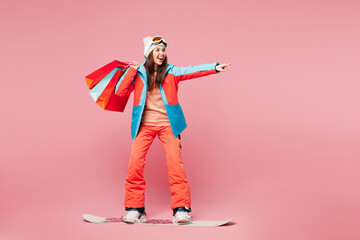 Full body young woman in blue padded jacket ski goggles mask spend weekend winter season in mountains ride snowboard hold shopping package bags isolated on plain pink background Sale buy day concept © ViDi Studio