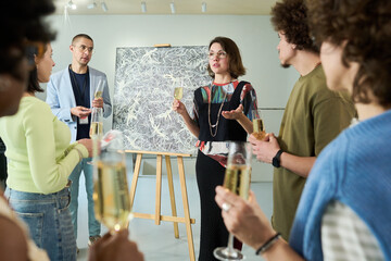 Young confident female artist with flute of champagne presenting her new artwork to intercultural...