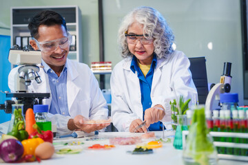 A female and male scientist conduct plant research in a laboratory, using microscopes, petri...