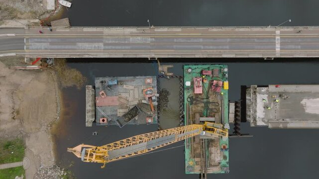 Aerial top down view of excavator machine building a bridge over Salaca river (Salacgriva city), dark autumn water, wide birdseye shot