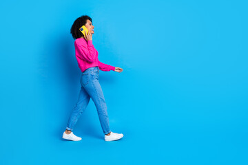 Full body photo of attractive young woman walk talk phone dressed stylish pink clothes isolated on blue color background