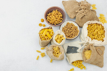 Pasta. Various kinds of uncooked pasta and noodles over light stone background. Traditional Italian