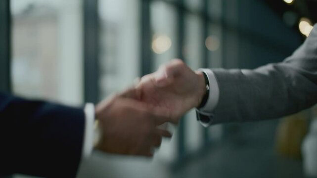 Handshake between two business executives wearing formal suits and wristwatches during meeting. Close-up shot, focus on foreground