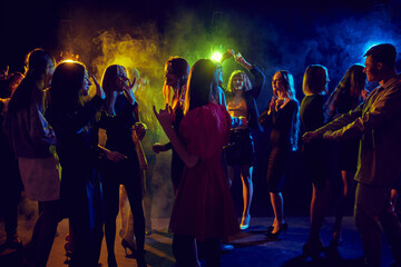 Group of young people attending party, cheerfully dancing, talking, having fun over dark background...