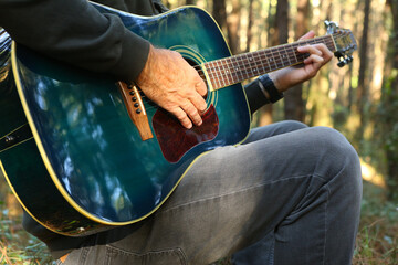 A man in the foreground playing acoustic guitar in the forest