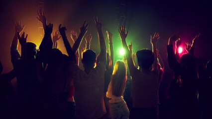 Back view of people, silhouettes, men and women attending concert of favorite band or singer, dancing with hands raised, singing. Concept of youth culture, party, fun and leisure