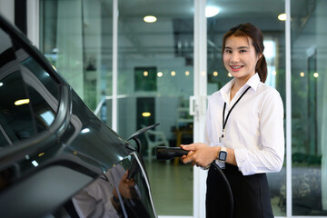 Smiling young woman connecting charging cable to an electric vehicle. Modern transportation concept