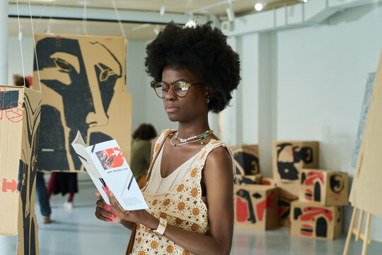 Contemporary young woman in eyeglasses and elegant attire looking through points of modern art exhibition