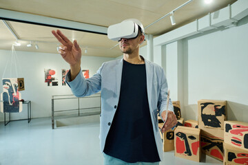 Young man in elegant blue suit and VR headset looking through interactive list of modern art...