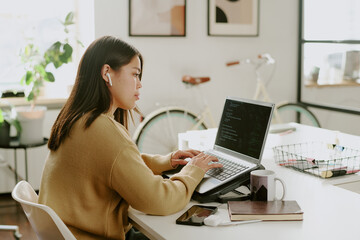 Profile of young adult office worker listening to music via wireless headphones while coding on...