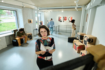 Serious young woman in elegant casualwear and eyeglasses looking at masterpiece of modern art in...