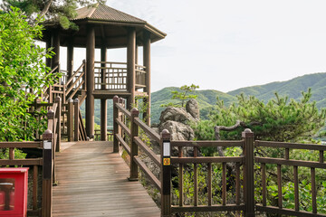 Fototapeta premium A wooden walkway with a wooden pavilion in the middle. The pavilion has a yellow sign on it. The walkway is surrounded by trees and has a peaceful, 