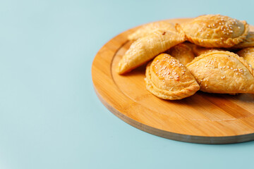 Freshly baked samsa pies with chicken sprinkled with sesame seeds on wooden plate, central asian cuisine.