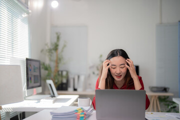 Young asian businesswoman struggling with a severe headache and feeling exhausted after spending...