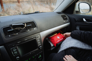 A person is currently seated inside a vehicle, specifically a car, which contains a first aid kit conveniently placed within the glovebox compartment for easy access during emergencies