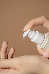 Person arm holding a bottle of hand sanitizer, beige background. Close-up, vertical frame