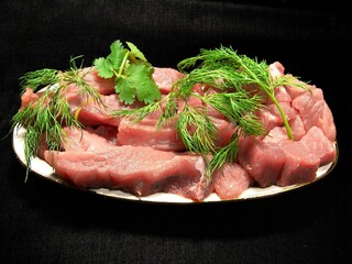 Raw uncooked meat with greens on a plate close view background